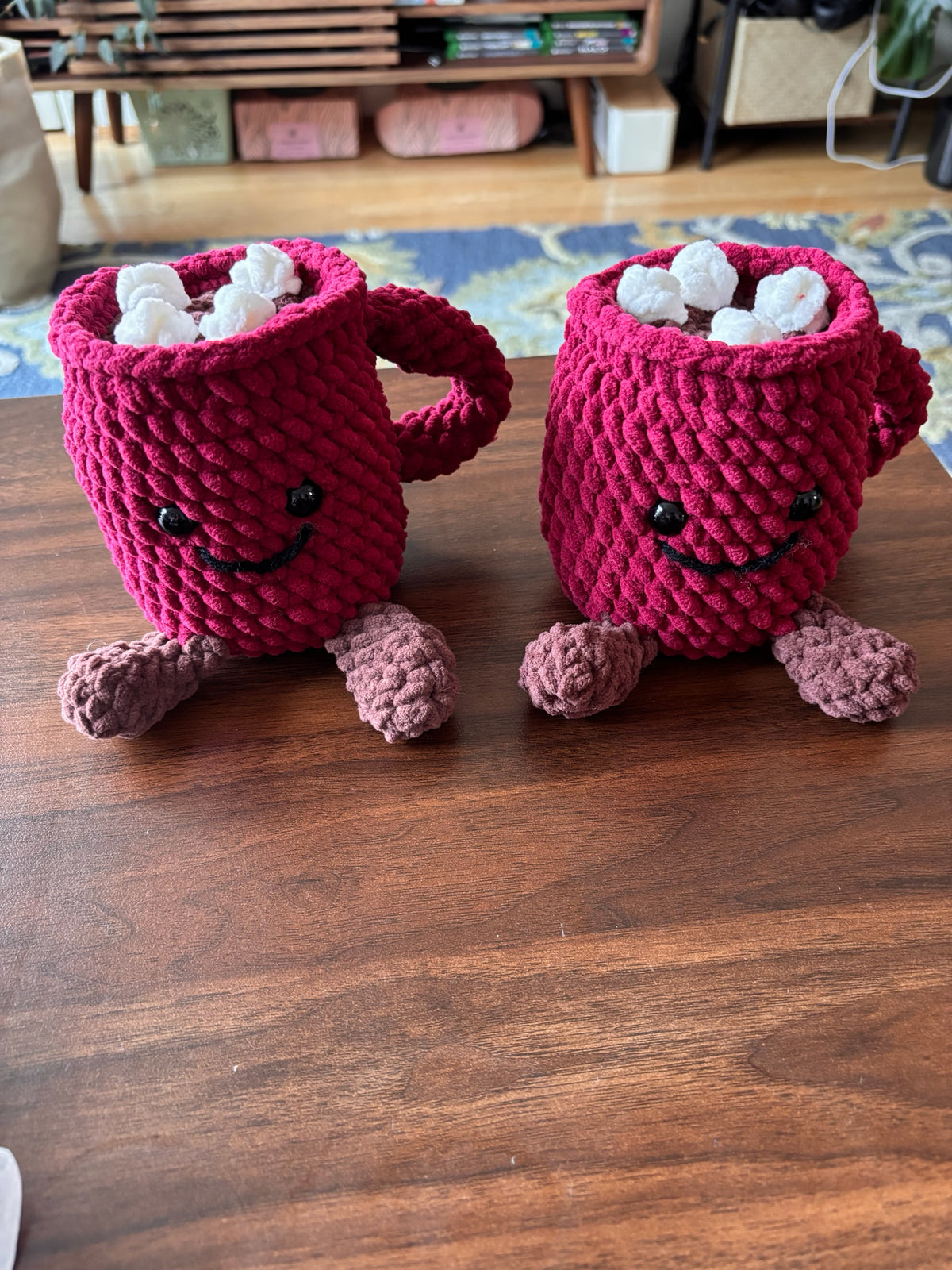 Hook Happy Co. handmade berry-red crochet hot cocoa mug plushies with white marshmallows and smiling faces.